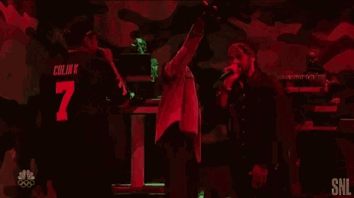 a group of people are standing on a stage in a dark room with a red light behind them .