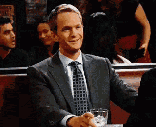 a man in a suit and tie is sitting at a table with a drink .