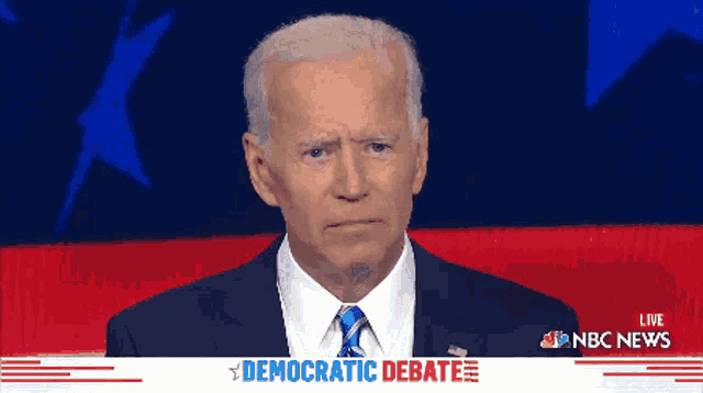 a man in a suit and tie stands in front of a screen that says democratic debate on it