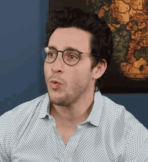 a man wearing glasses and a polka dot shirt looks to his left