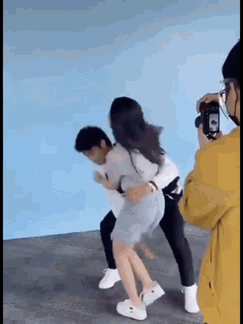 a man is carrying a woman on his back while a woman takes a picture of them .