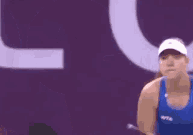 a woman in a blue tank top is holding a tennis racquet in front of a sign that says per