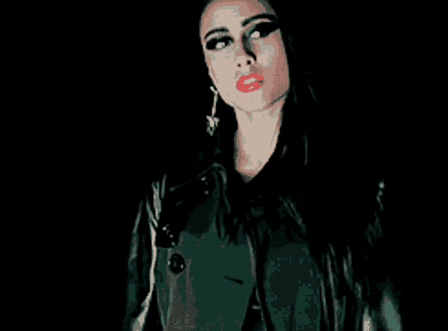 a woman wearing a trench coat and red lipstick is standing in the dark