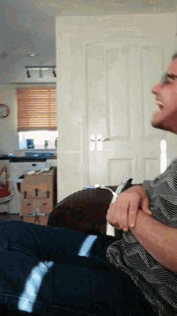 a man in a striped shirt is sitting on a couch and laughing