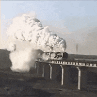 a train is going over a bridge with lots of smoke coming out of it .