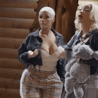 two women are standing next to each other in front of a log cabin holding a teddy bear .