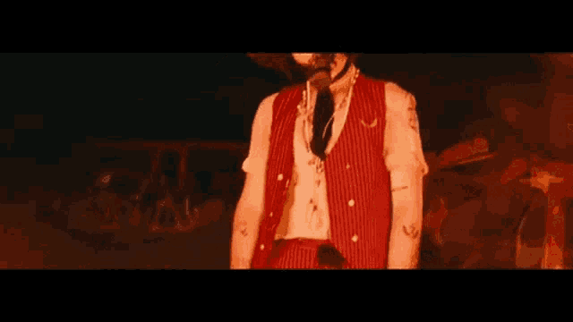 a man in a red striped vest and tie is standing in the dark .