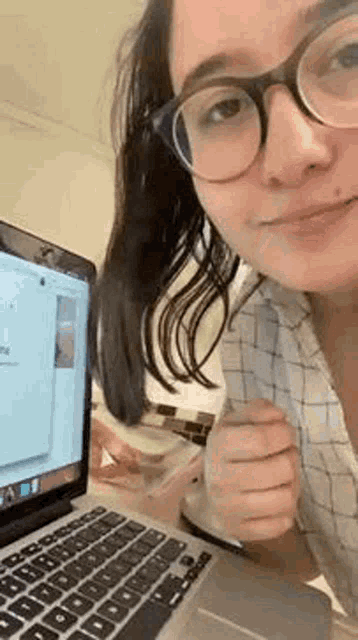a woman wearing glasses is sitting at a desk with a laptop computer .