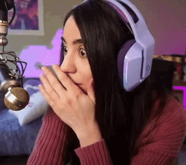 a woman wearing headphones covering her mouth while sitting in front of a microphone