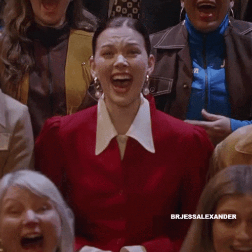 a woman in a red jacket is laughing in a crowd of people with the name brjessalexander on the bottom