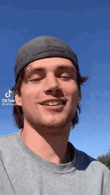 a young man wearing a hat and a gray shirt is smiling .