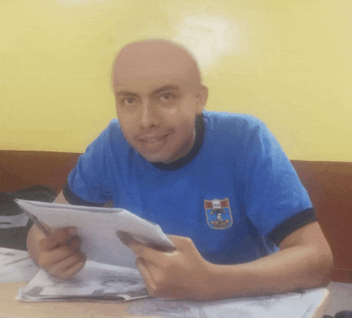 a man wearing a blue shirt with a crest on it is holding a piece of paper