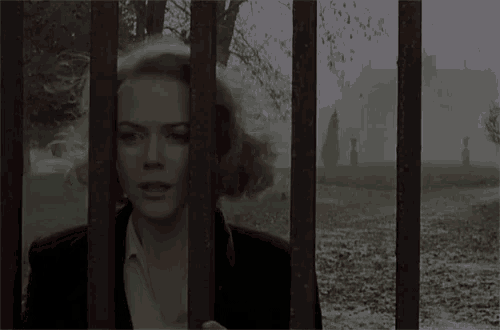 a woman is standing behind a fence in a cemetery in the fog .