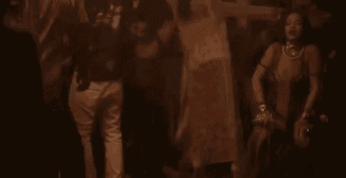 a woman is dancing in a dark room with a group of people standing around her .