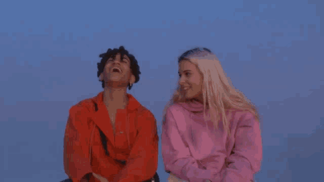 a man in a red jacket and a woman in a pink sweater are laughing together