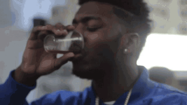 a man in a blue shirt is drinking from a small glass