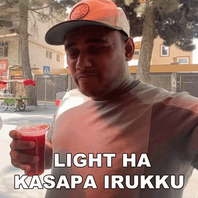 a man wearing a hat holds a glass of red liquid and says light ha kasapa irukku