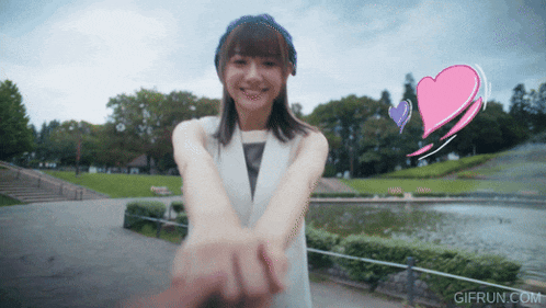 a woman holds a man 's hand in a park with a pink heart behind her