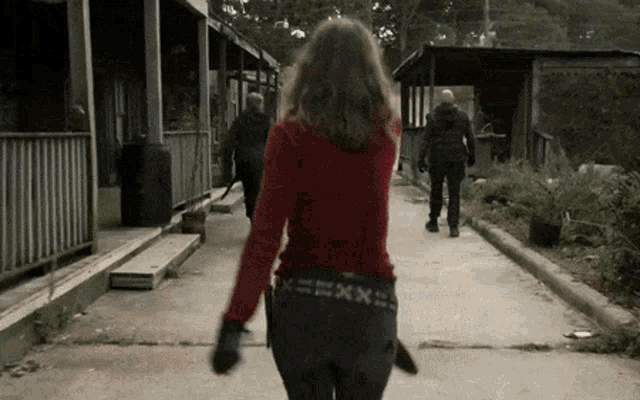 a woman in a red sweater is walking down a street holding a knife