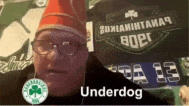 a man wearing glasses and a red hat is standing in front of a banner that says underdog