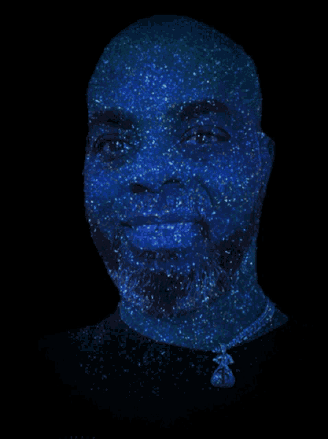 a man 's face is covered in blue sparkles with a necklace around his neck