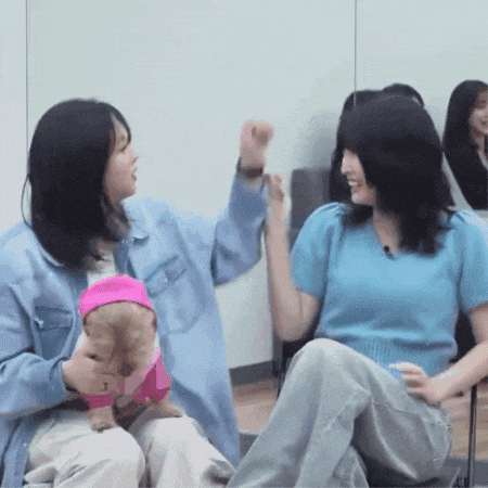 two women are sitting next to each other and one is holding a small dog in a pink outfit .
