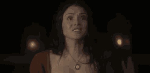 a woman is standing in the dark wearing a necklace and looking at the camera .
