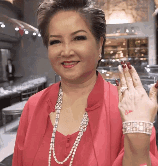 a woman wearing a pink jacket and a pearl necklace shows off her ring