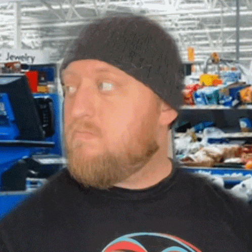 a man with a beard wearing a beanie and a black shirt in a store with a sign that says jewelry