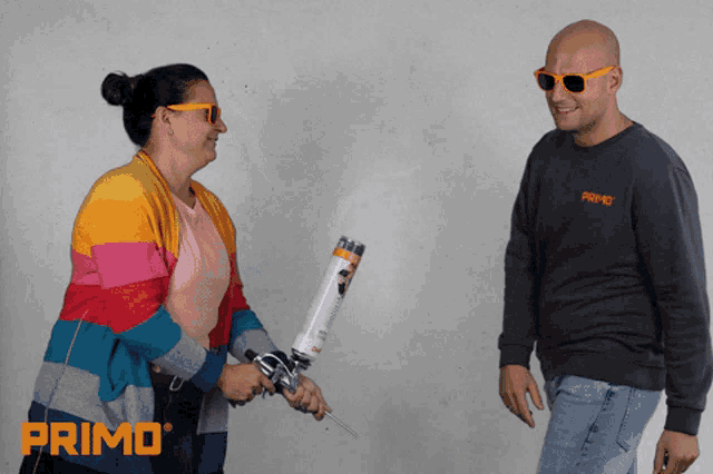 a man wearing sunglasses and a sweater that says primo stands next to a woman holding a spray gun