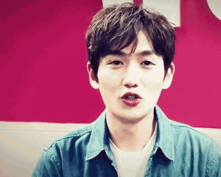 a young man wearing a denim shirt and a white t-shirt looks at the camera
