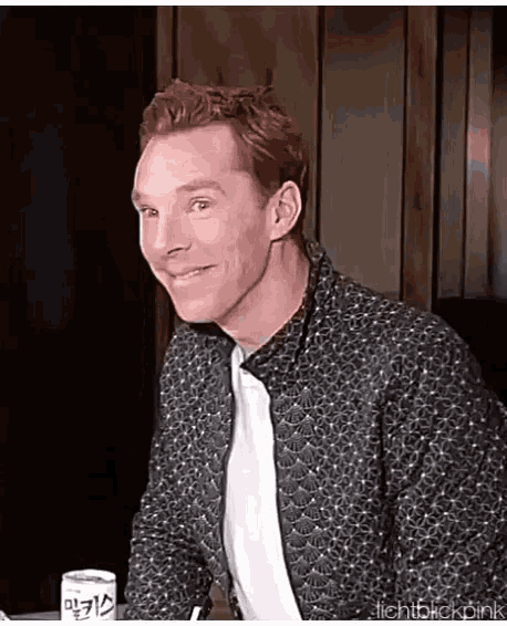 a man is sitting at a table and smiling while wearing a jacket .