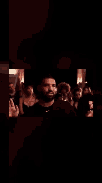 a man with a beard is standing in front of a crowd with his hands in the air .
