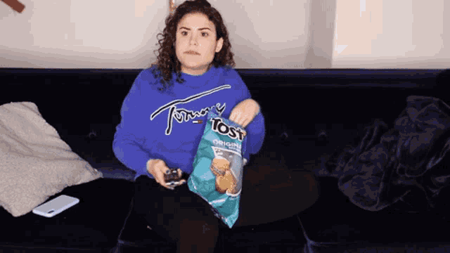 a woman is sitting on a couch with a bag of tost chips