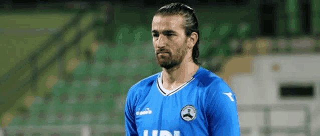 a man with a beard is wearing a blue soccer jersey on a field .