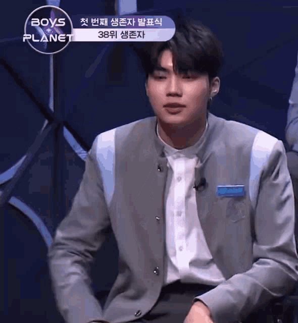 a man in a suit is sitting in front of a sign that says boys planet .