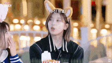 a girl wearing a dog ear headband is eating popcorn while another girl looks on .