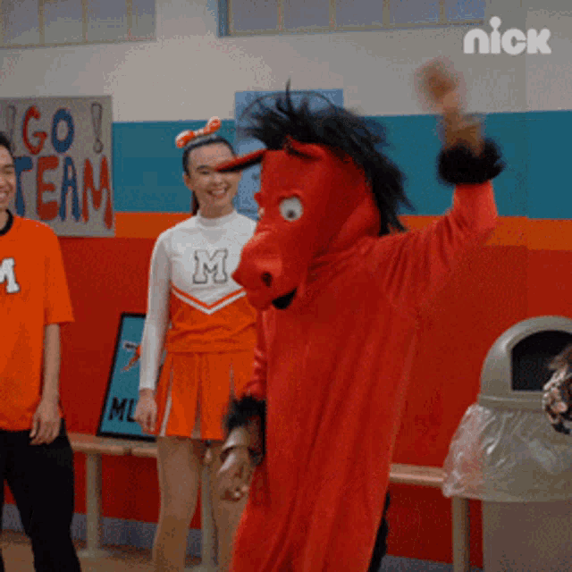 a man in a red horse costume stands in front of a sign that says " go team "