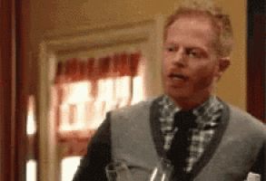 a man in a sweater vest and tie is holding a glass of wine .