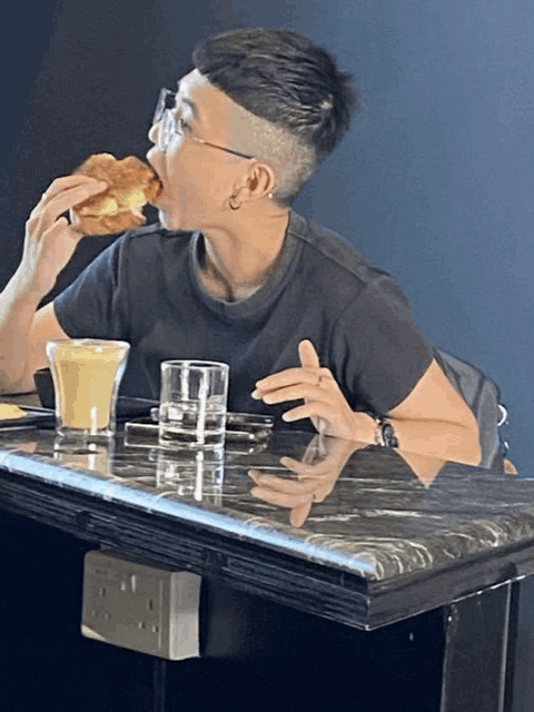 a man sitting at a table eating a croissant and drinking a milkshake