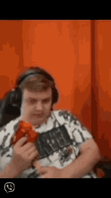a man wearing headphones is holding a red object in front of an orange wall .