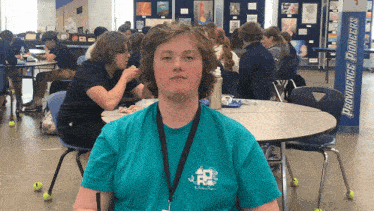 a boy wearing a providence pioneers shirt sits at a table in a cafeteria