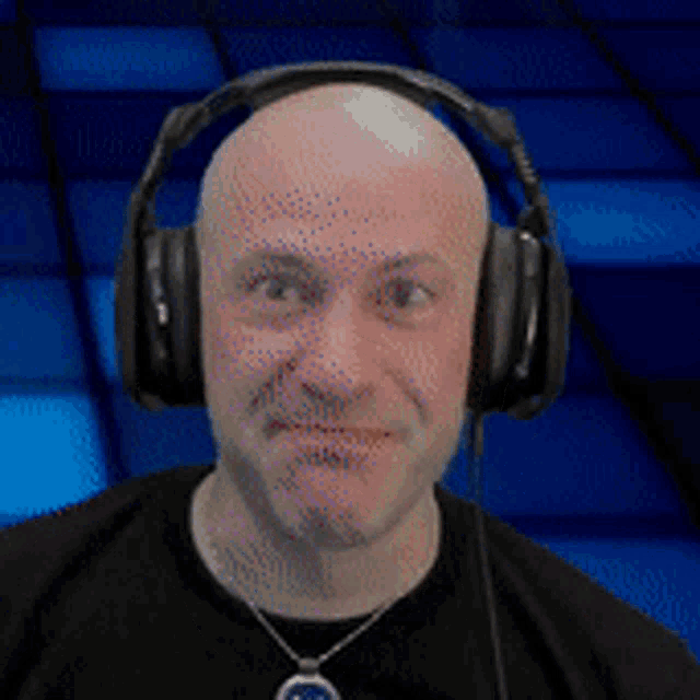 a bald man wearing headphones and a necklace is smiling