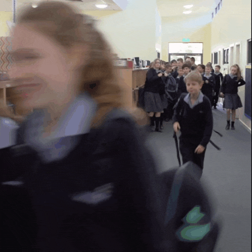 a group of children are walking down a hallway with their backpacks on