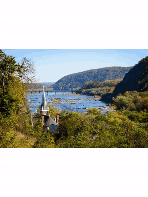 a church with a steeple overlooking a river with a bridge in the distance