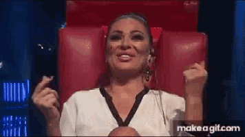 a woman in a white shirt is sitting in a red chair with her hands in the air .