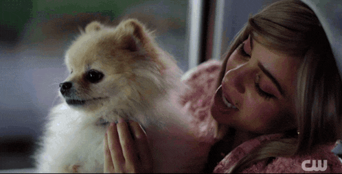 a woman holding a small white dog with the cw logo visible