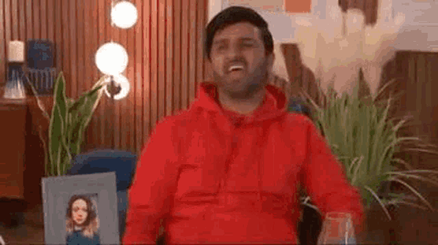 a man in a red hoodie is sitting in a chair with a glass of wine and a picture of a woman .