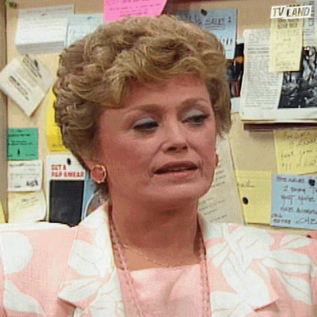 a woman stands in front of a bulletin board with sticky notes on it including one that says get a flip phone