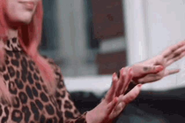 a woman with pink hair is wearing a leopard print shirt and has a tattoo on her hand .